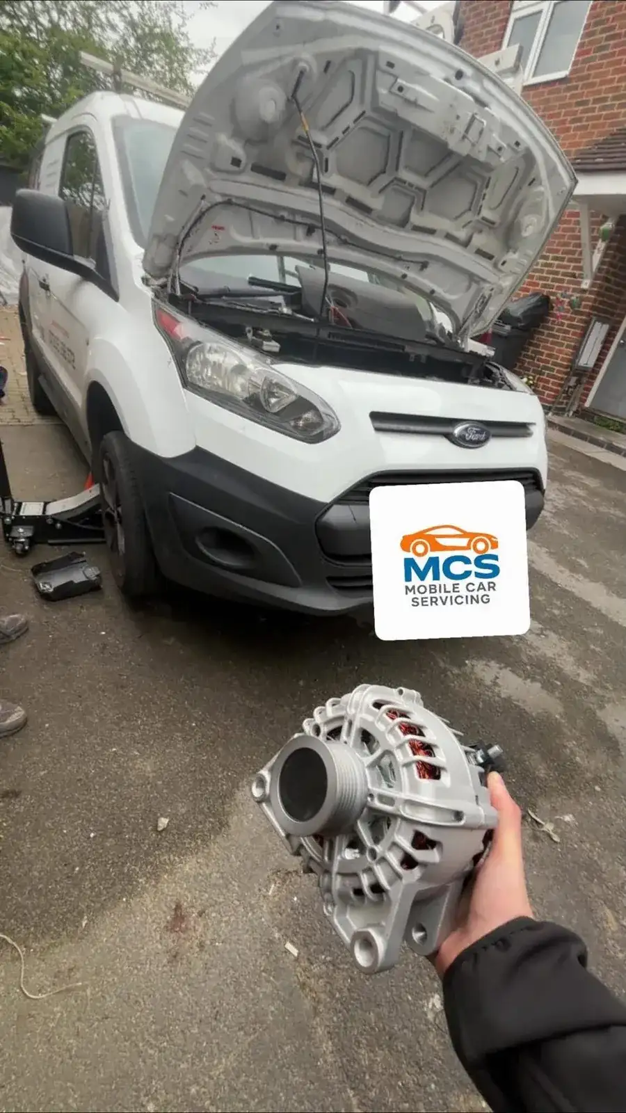 Mechanic holding a replacement alternator in front of an open van bonnet