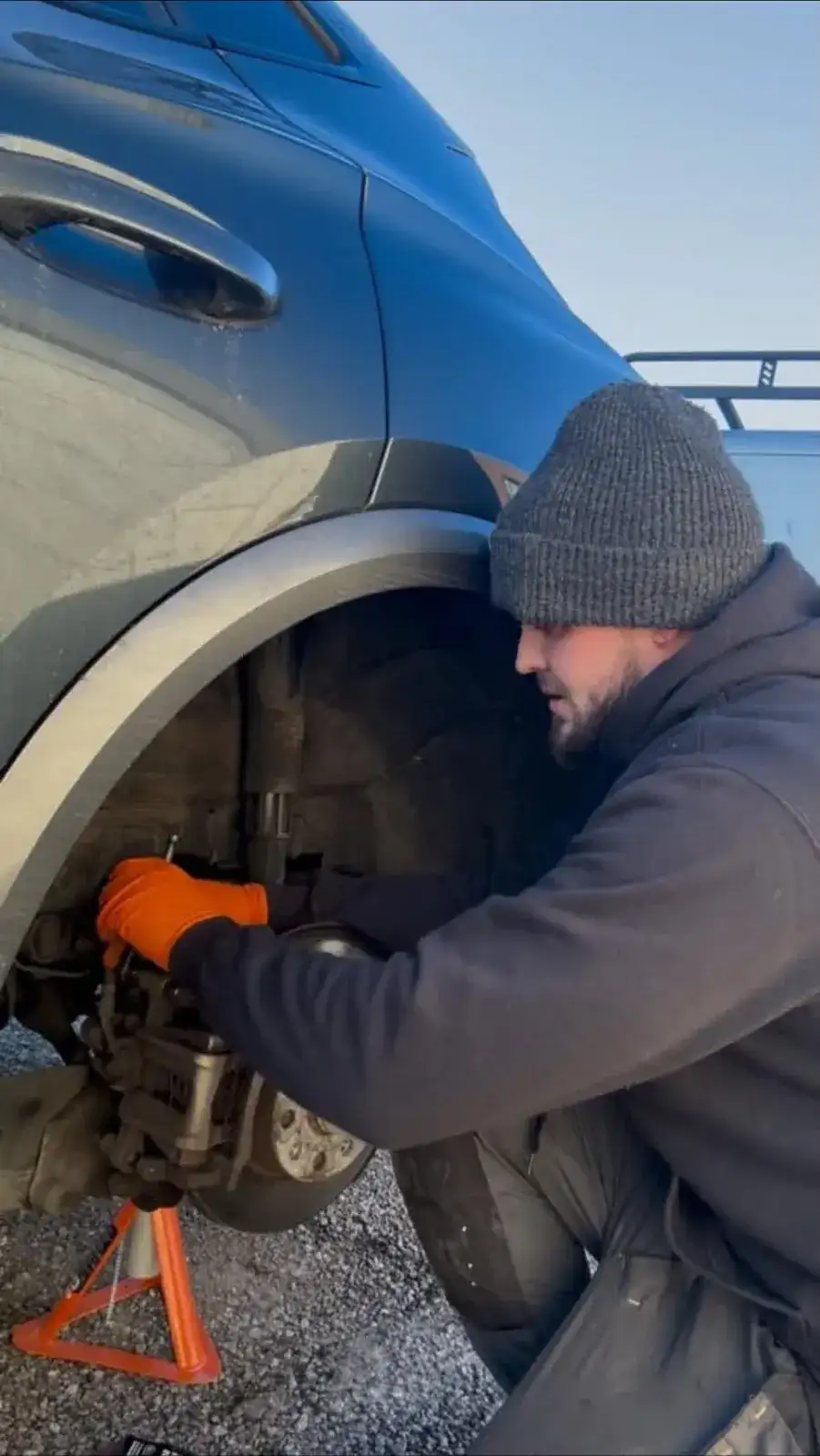 Mechanic working on a brake caliper under a car's wheel arch