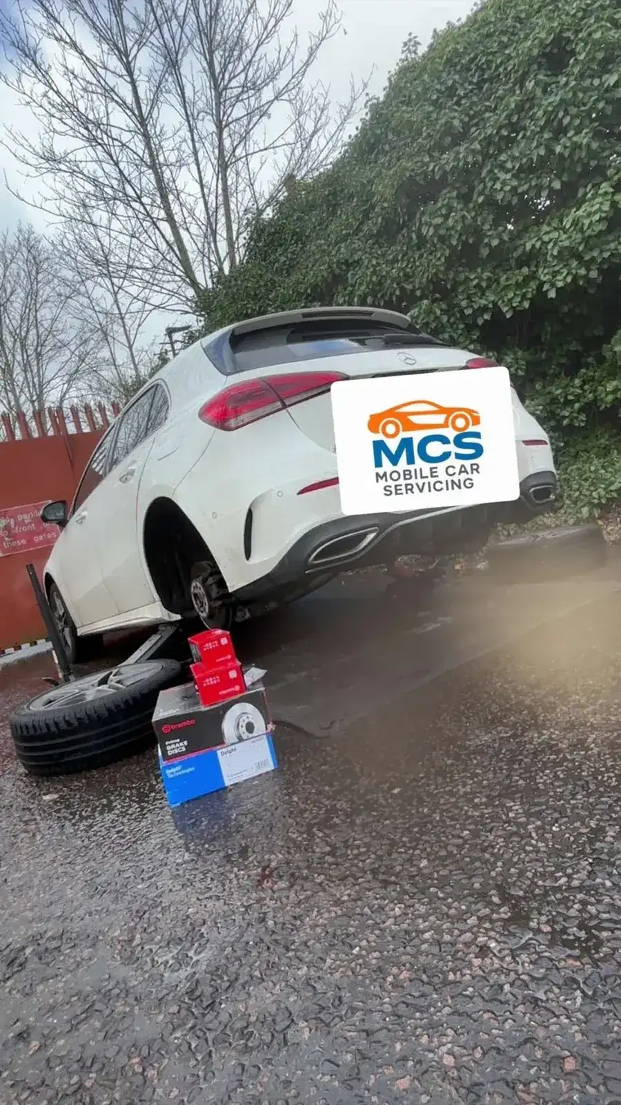 Mercedes raised for a brake job, new discs and pads boxed on the ground